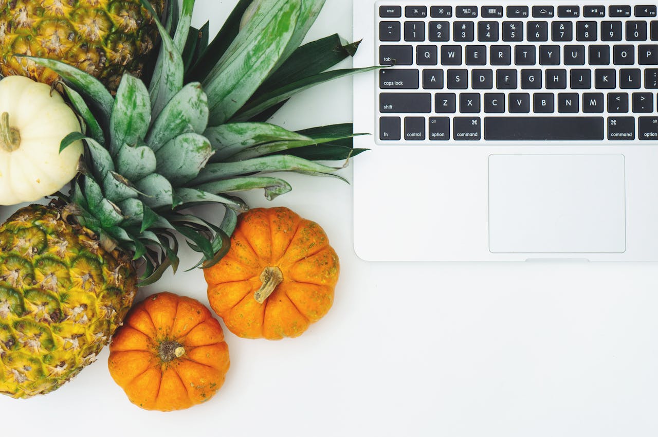 A top view of pineapples, pumpkins, and a laptop on a clean white background.